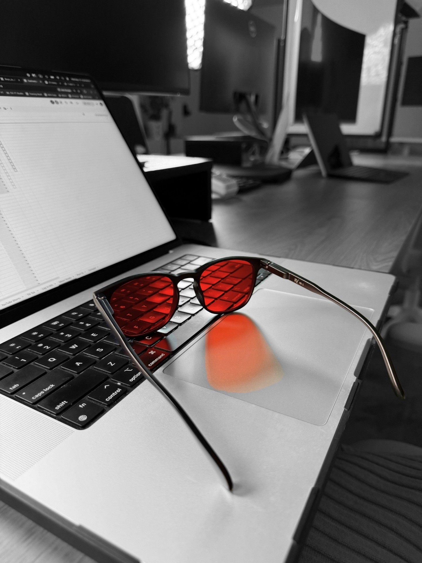 Kronveil red-lens glasses resting on a MacBook keyboard in a dark office